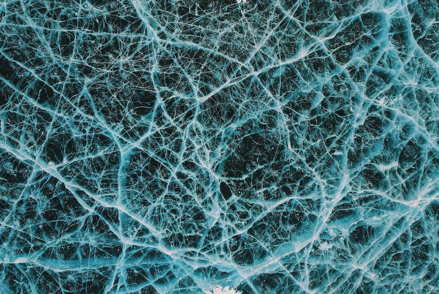 Close-up of cracked ice with intricate, web-like patterns and frost on the surface.