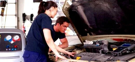 Two mechanics examining a car engine in a garage workshop.