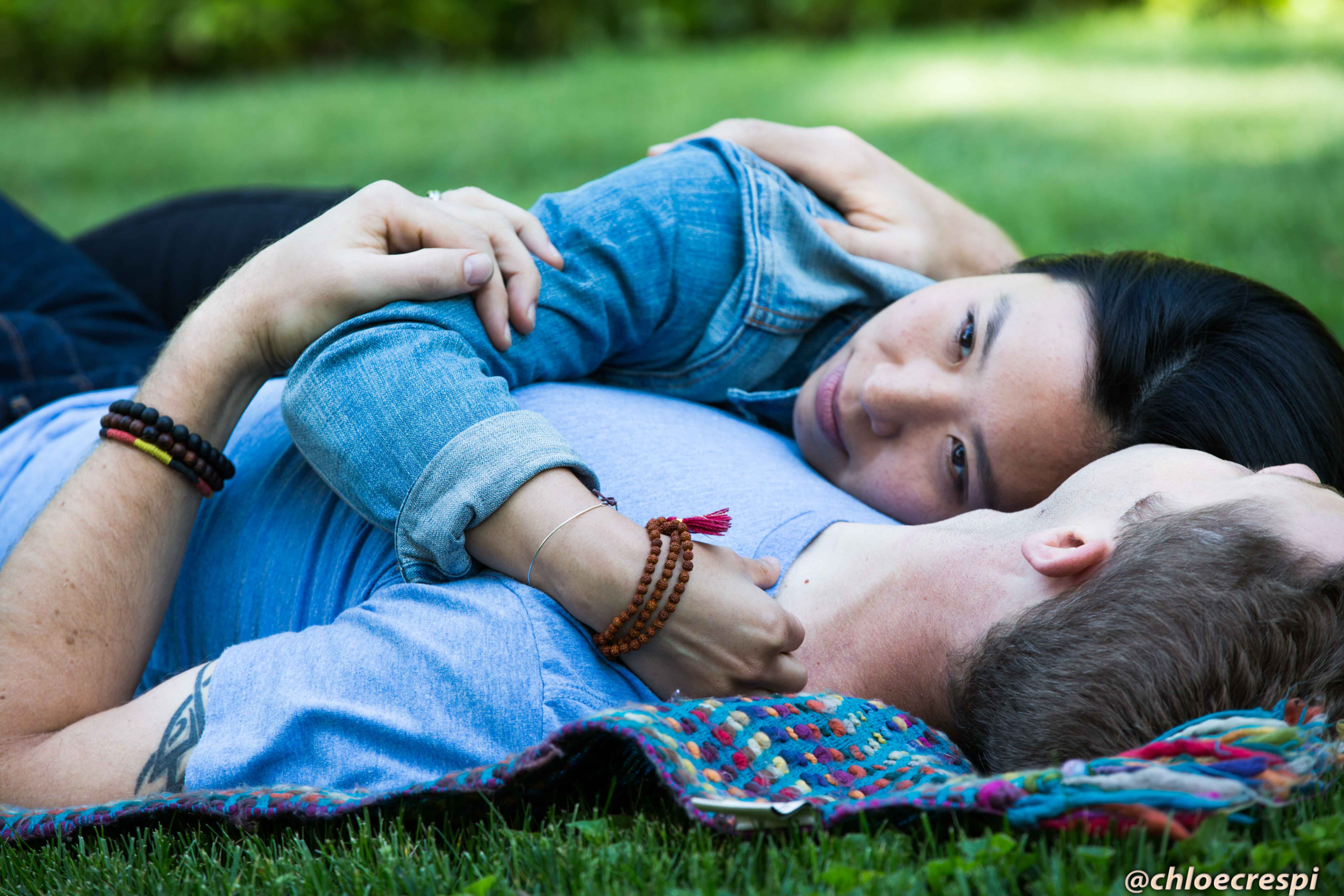 Couple lying on a blanket in the grass, embracing and looking at each other.