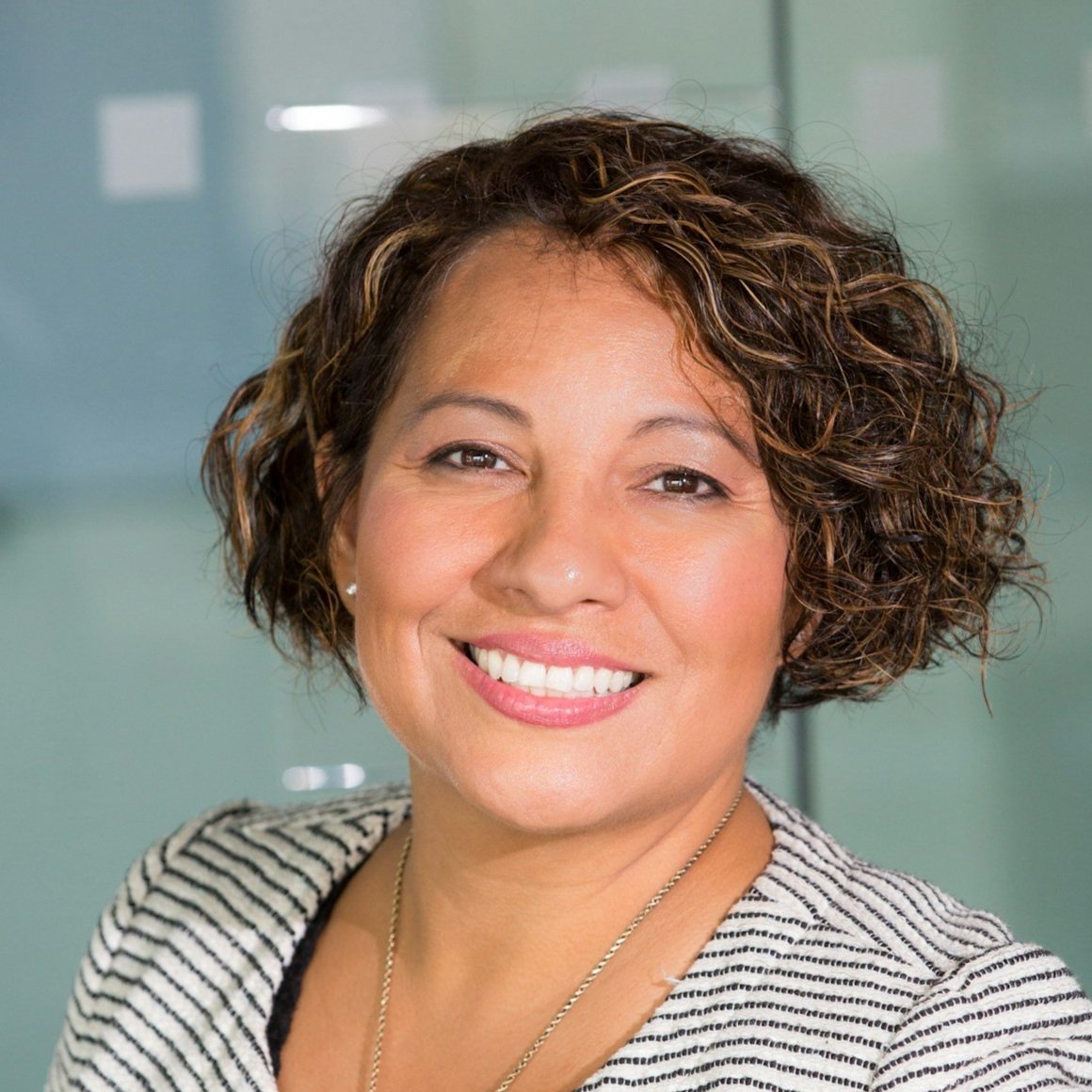 Smiling woman with curly hair wearing striped blazer in an office setting