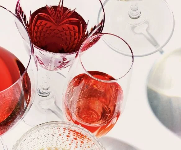 Several glasses of red wine on a white table, with a mix of different glass shapes and a white pitcher visible.
