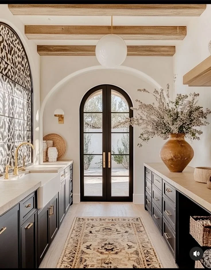Warm Mediterranean-inspired kitchen with arched doors, black cabinets, gold fixtures, and natural wood accents
