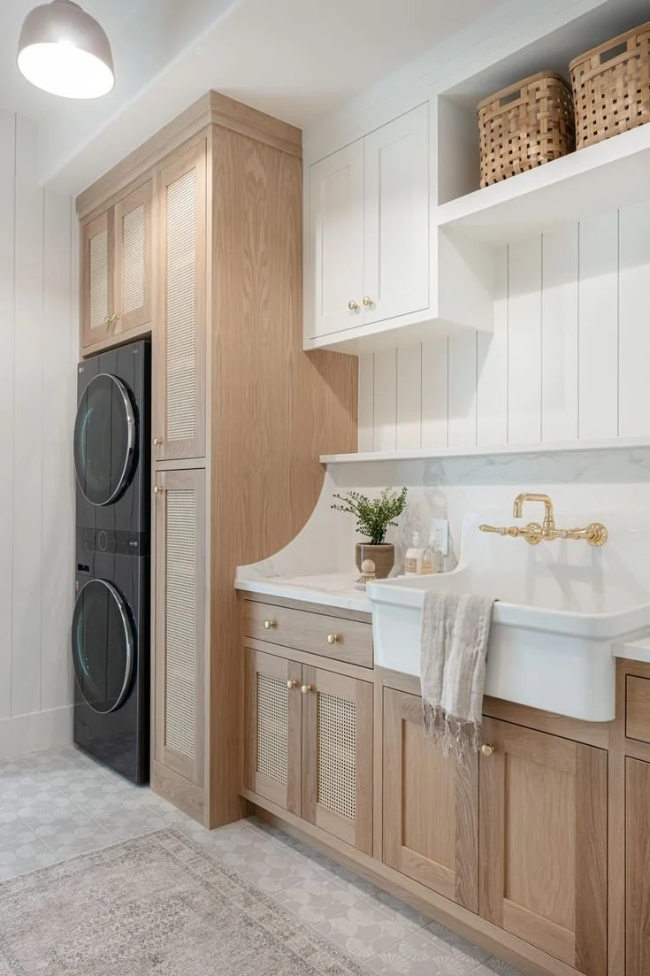 Modern farmhouse laundry room with white and wood cabinetry, apron sink, and gold hardware