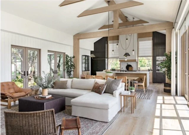 Open concept modern farmhouse kitchen and living area with vaulted ceiling, wood beams, and neutral palette.