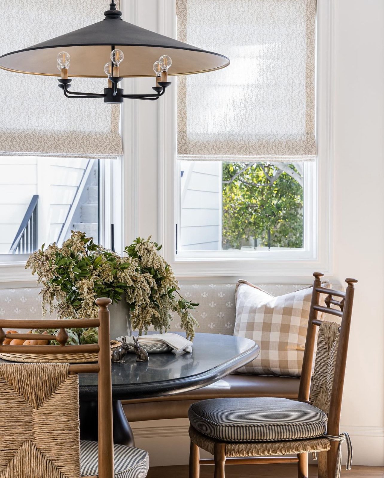 Cozy breakfast nook with built-in bench seating, round table, checkered pillows, and modern black chandelier.