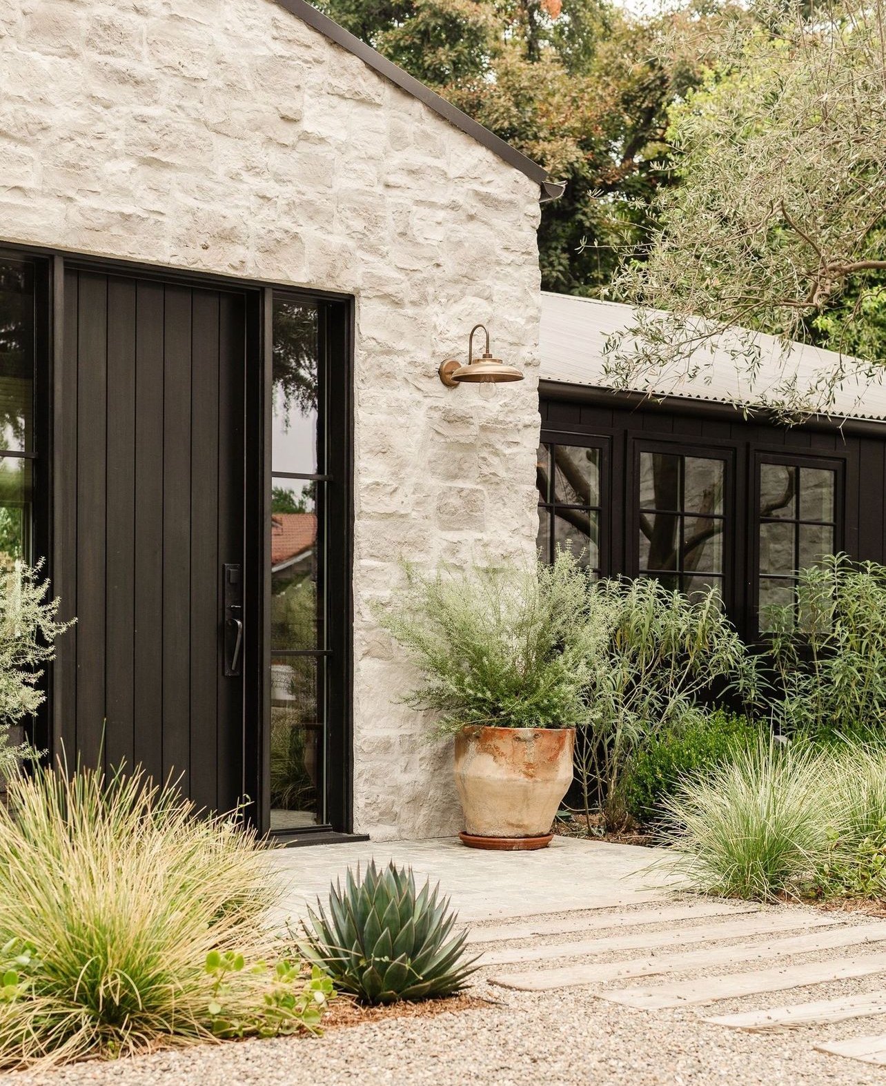 Modern rustic exterior with white stone walls, black framed windows and doors, and drought-tolerant landscaping.