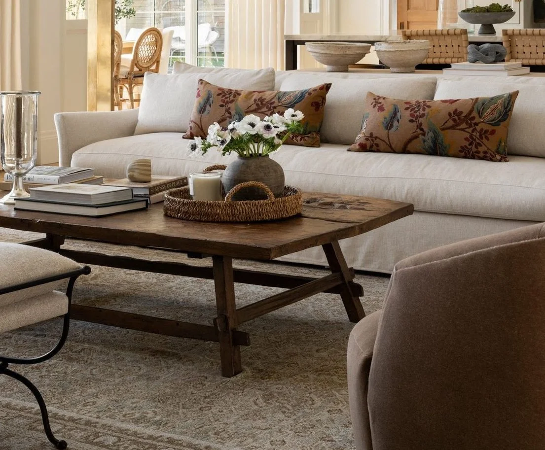 Earth-toned living room with neutral sofa, wooden coffee table, floral accent pillows, and layered vintage rug.