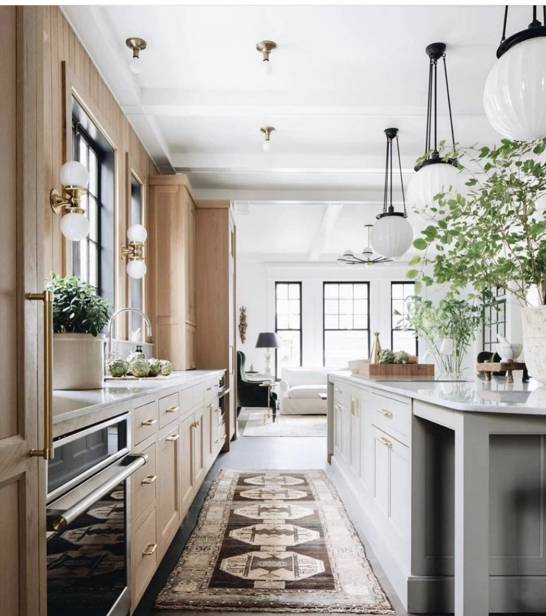 Transitional kitchen design with natural wood cabinetry, brass and black hardware, oversized pendant lighting, and a runner rug.