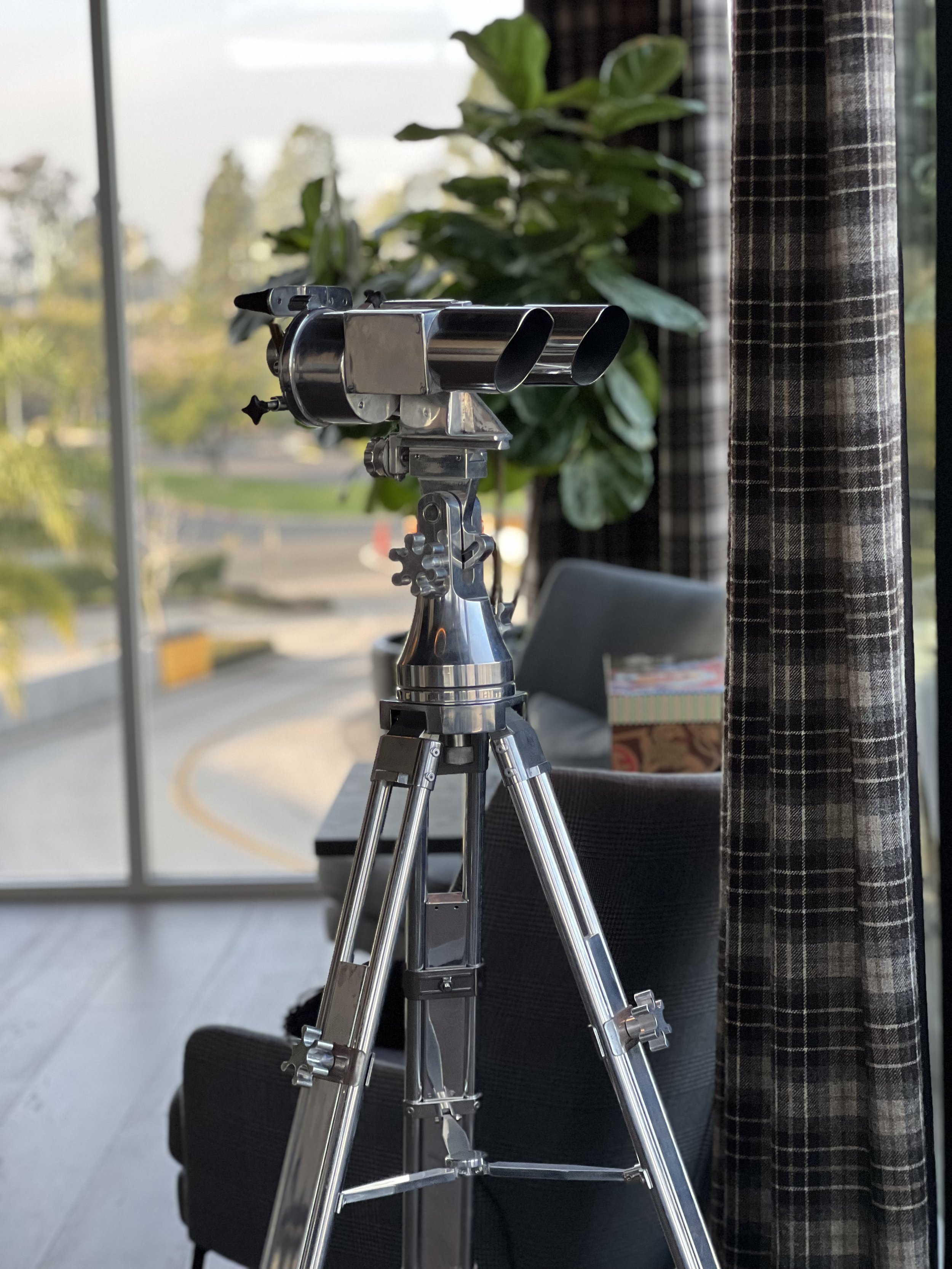 Polished metal telescope by office window with panoramic view and luxury interior seating