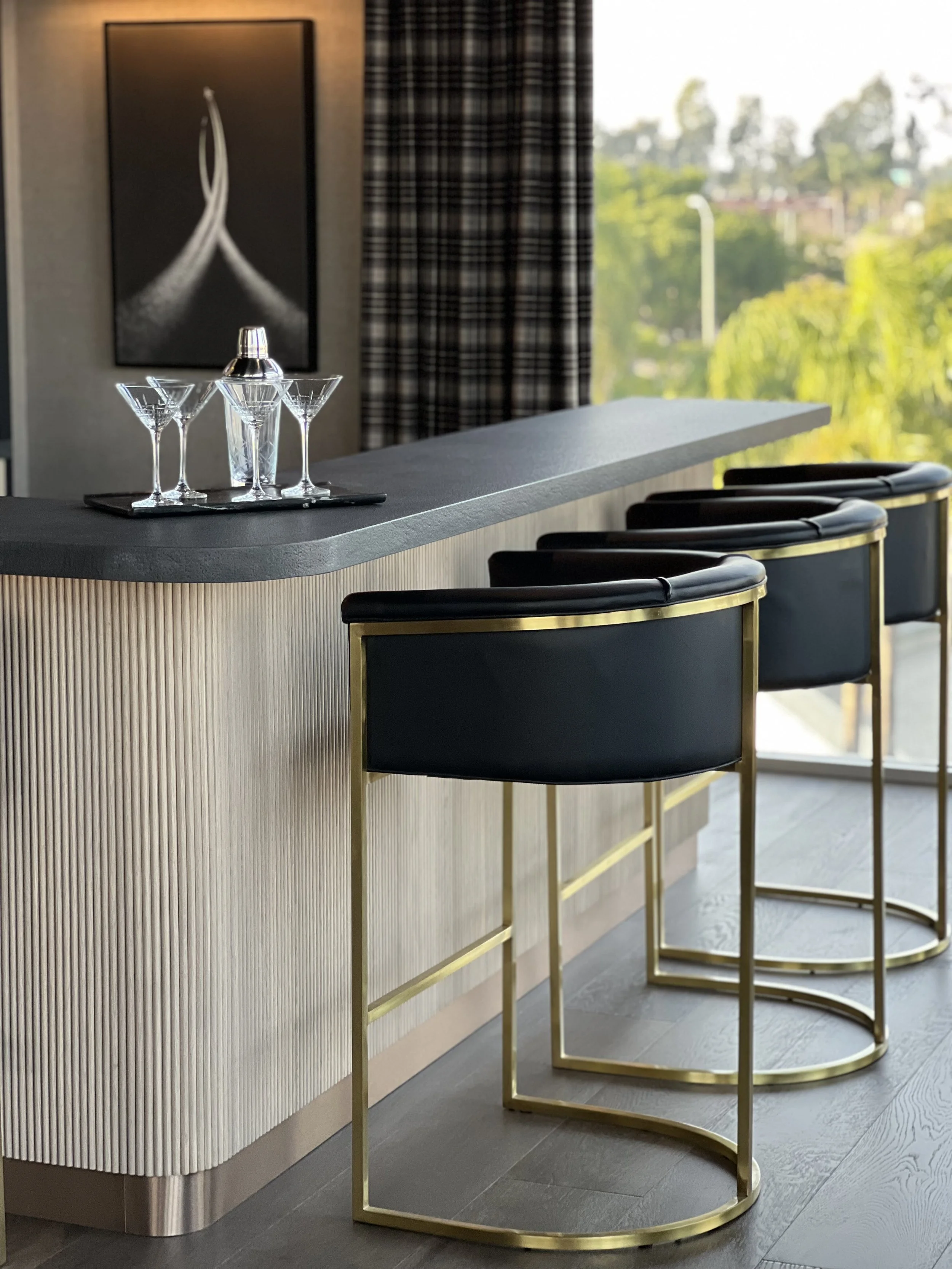 Elegant office bar counter with martini glasses, gold trim stools, and natural light from large windows
