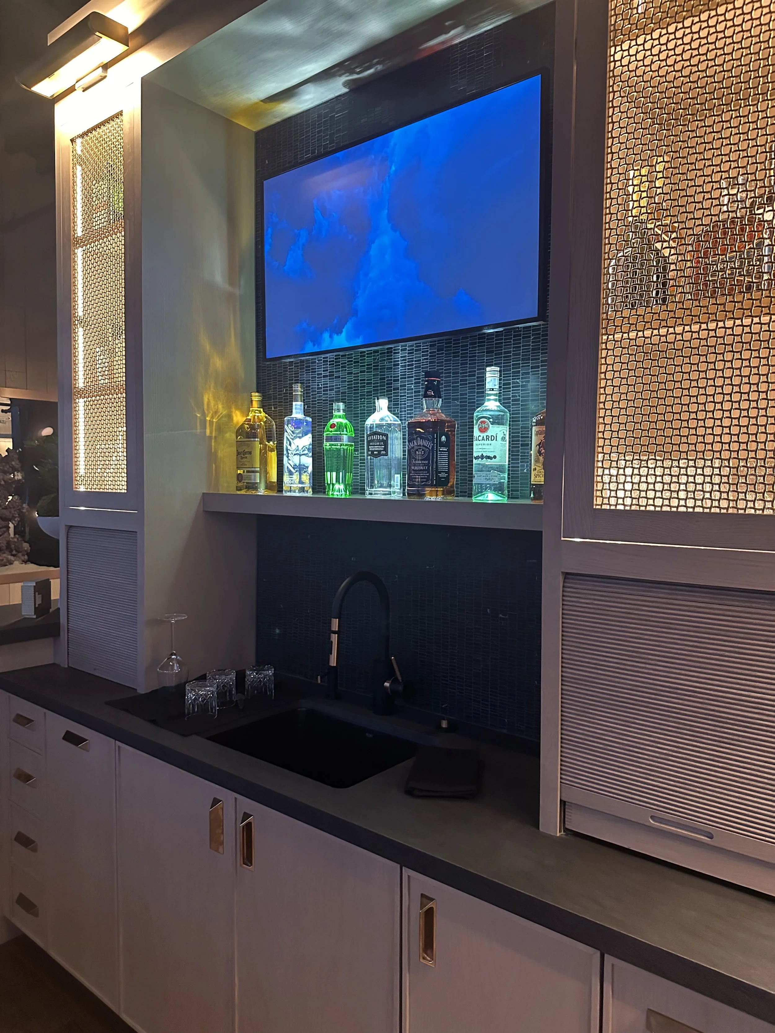 Executive office bar with modern sink, liquor display, ambient lighting, and mounted screen