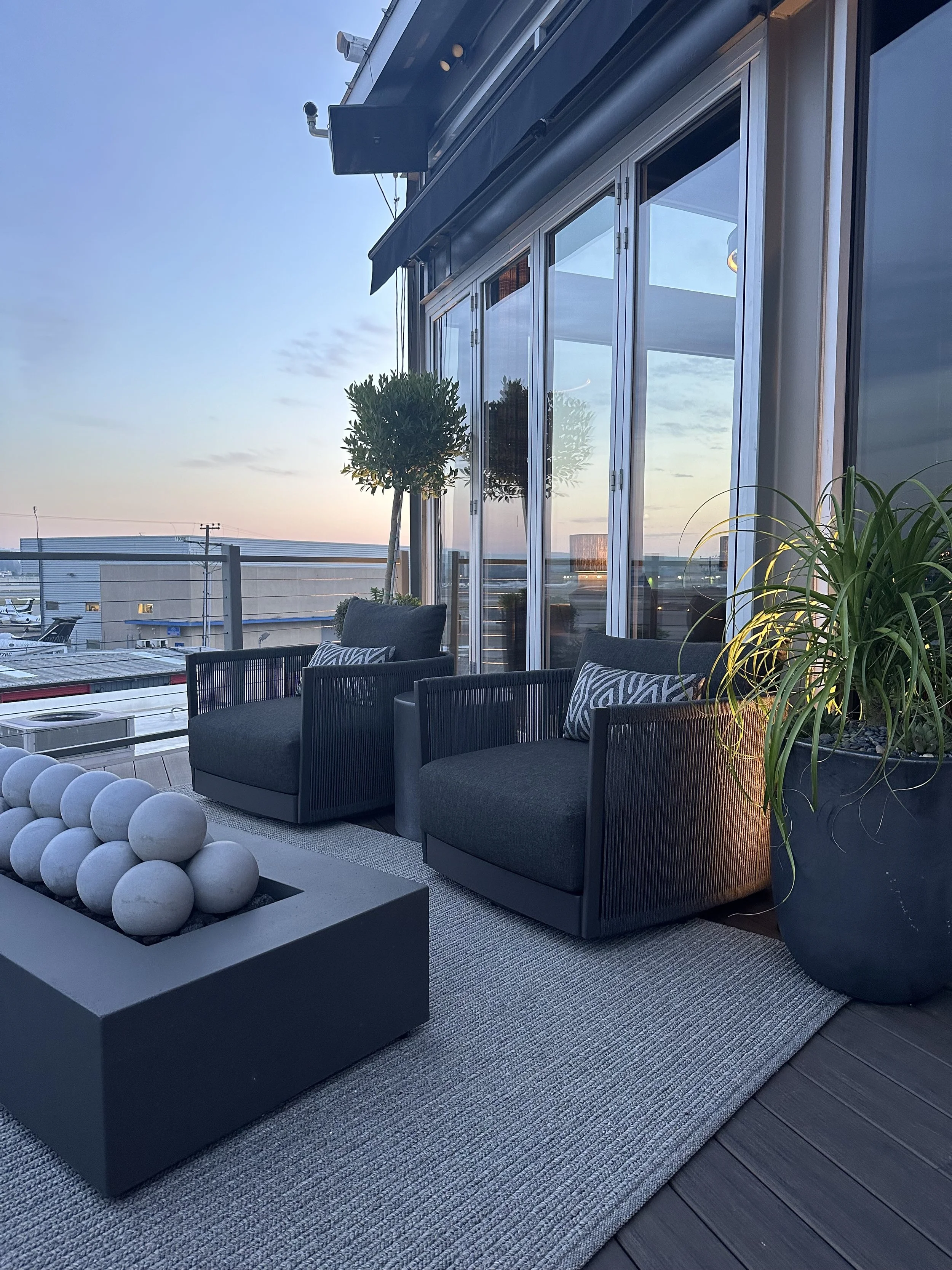 Elegant rooftop office terrace with modern black lounge chairs, sculptural fire  pit, and sunset view