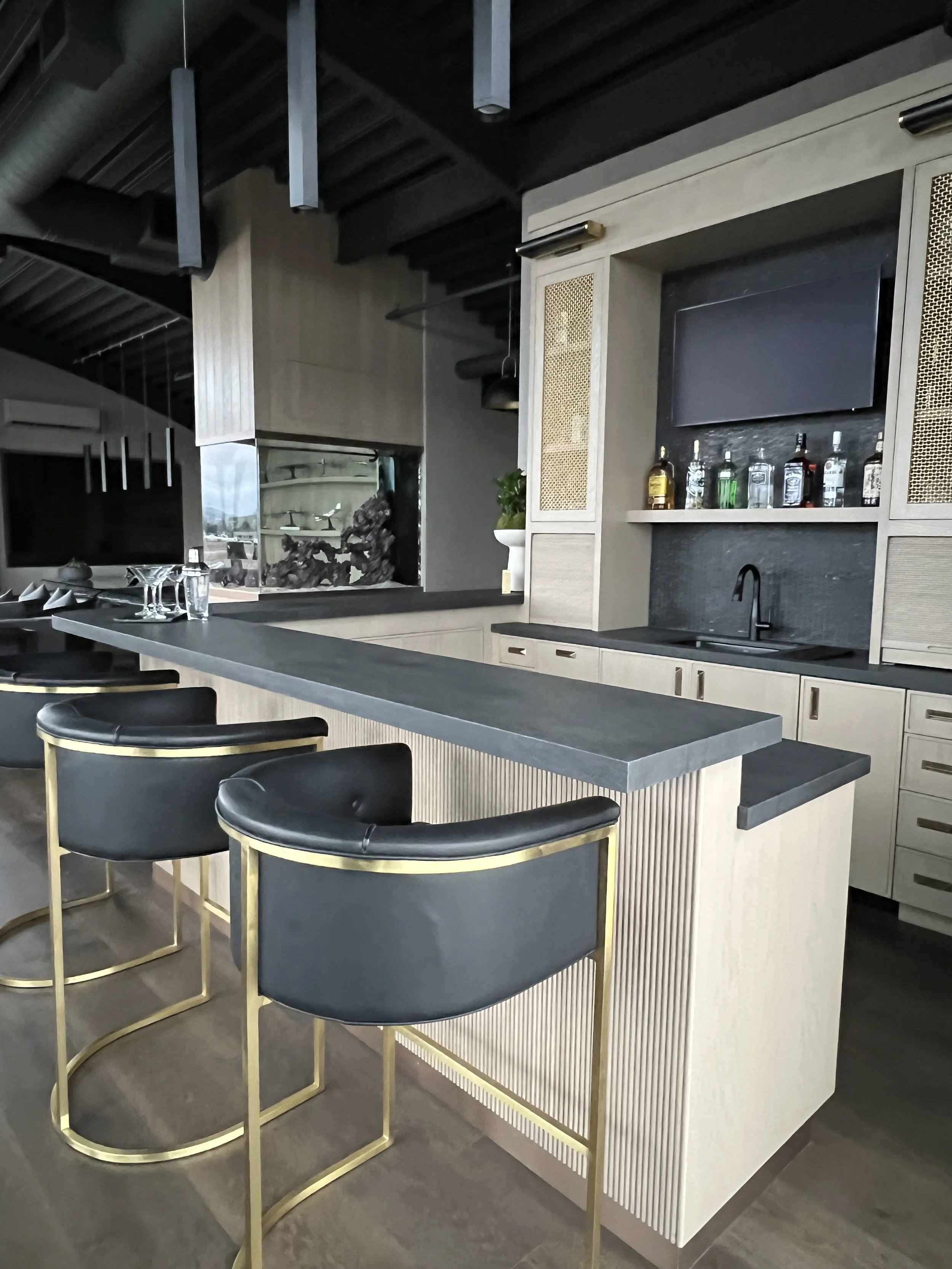 Luxury executive bar with modern shelving, green digital display, and black leather barstools with gold trim