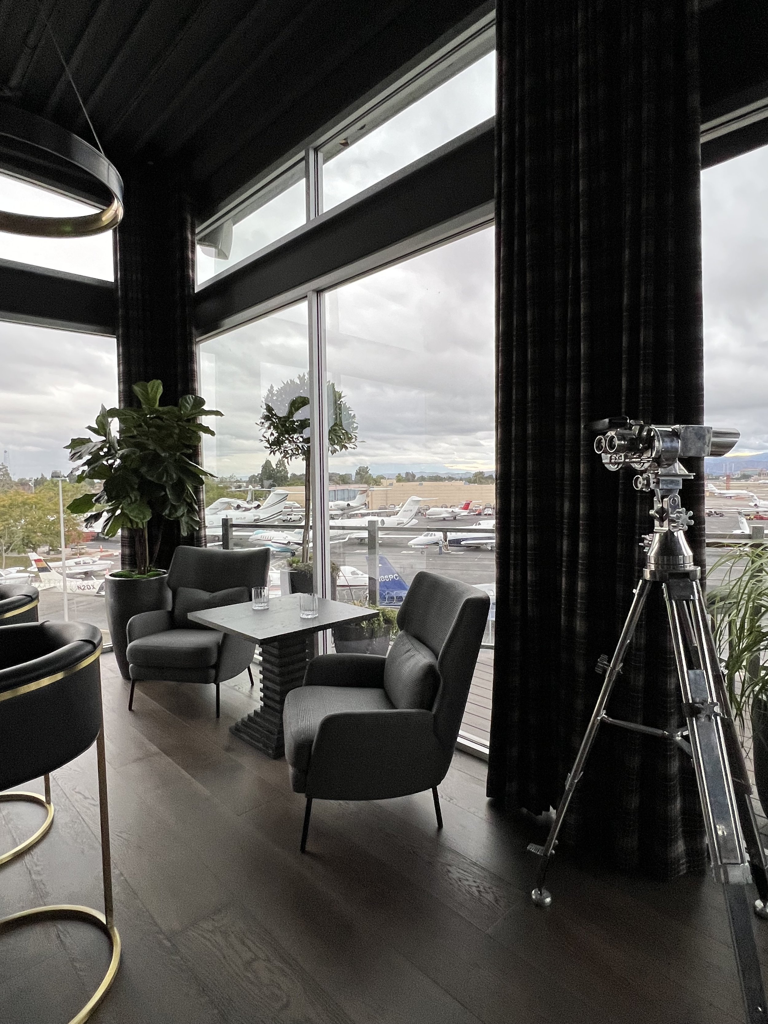 Cozy lounge nook with modern chairs, side table, telescope, and panoramic airport view from CEO office
