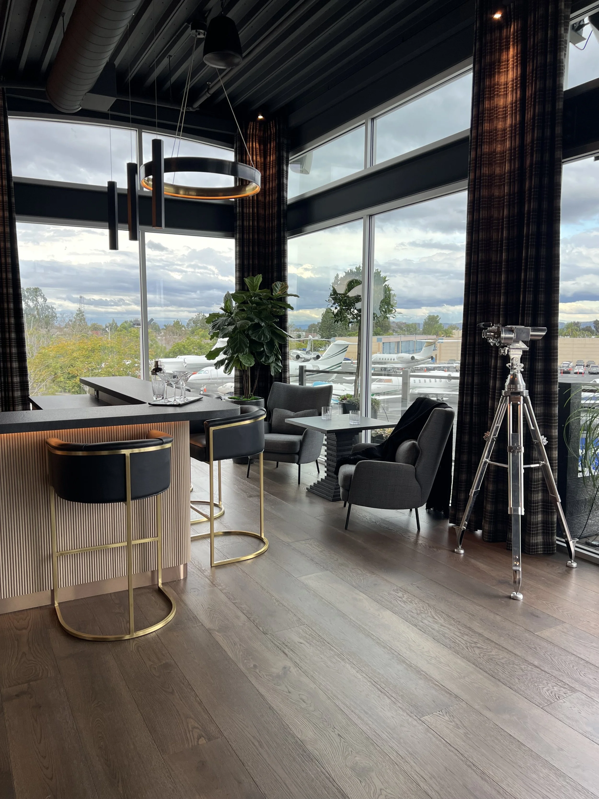 Luxury office bar with gold barstools, floor-to-ceiling windows, and private jet view from executive lounge
