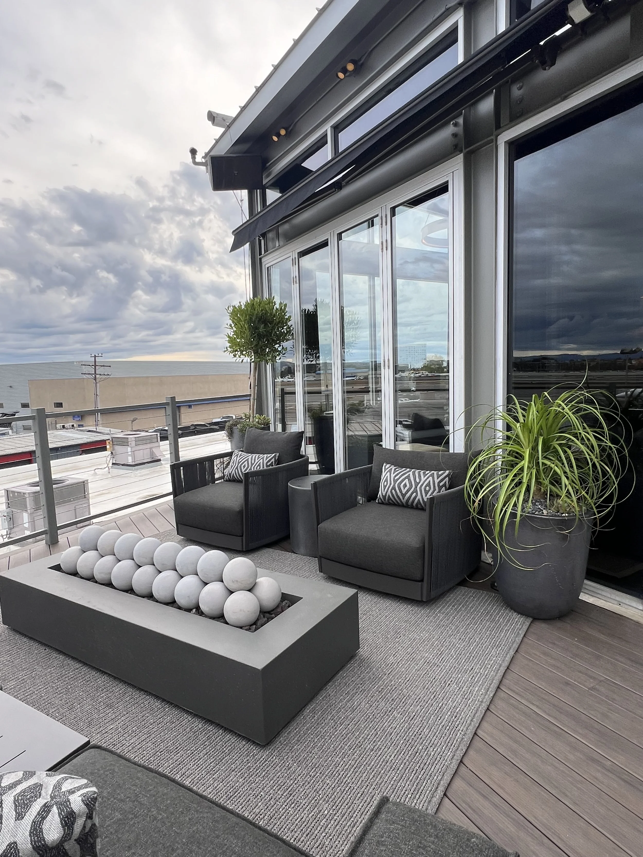 Luxury outdoor seating area with firepit, glass doors, potted plants, and panoramic office terrace views