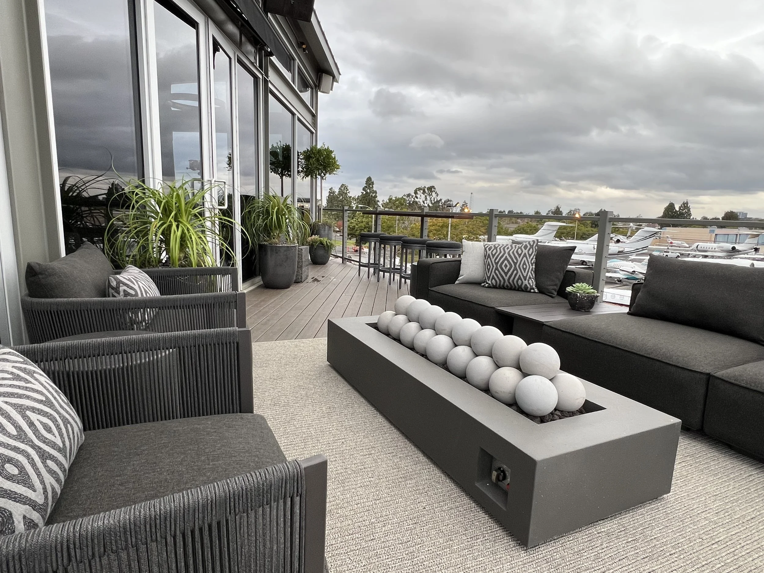 Modern rooftop lounge with firepit, black patio furniture, and private jet runway view at executive office
