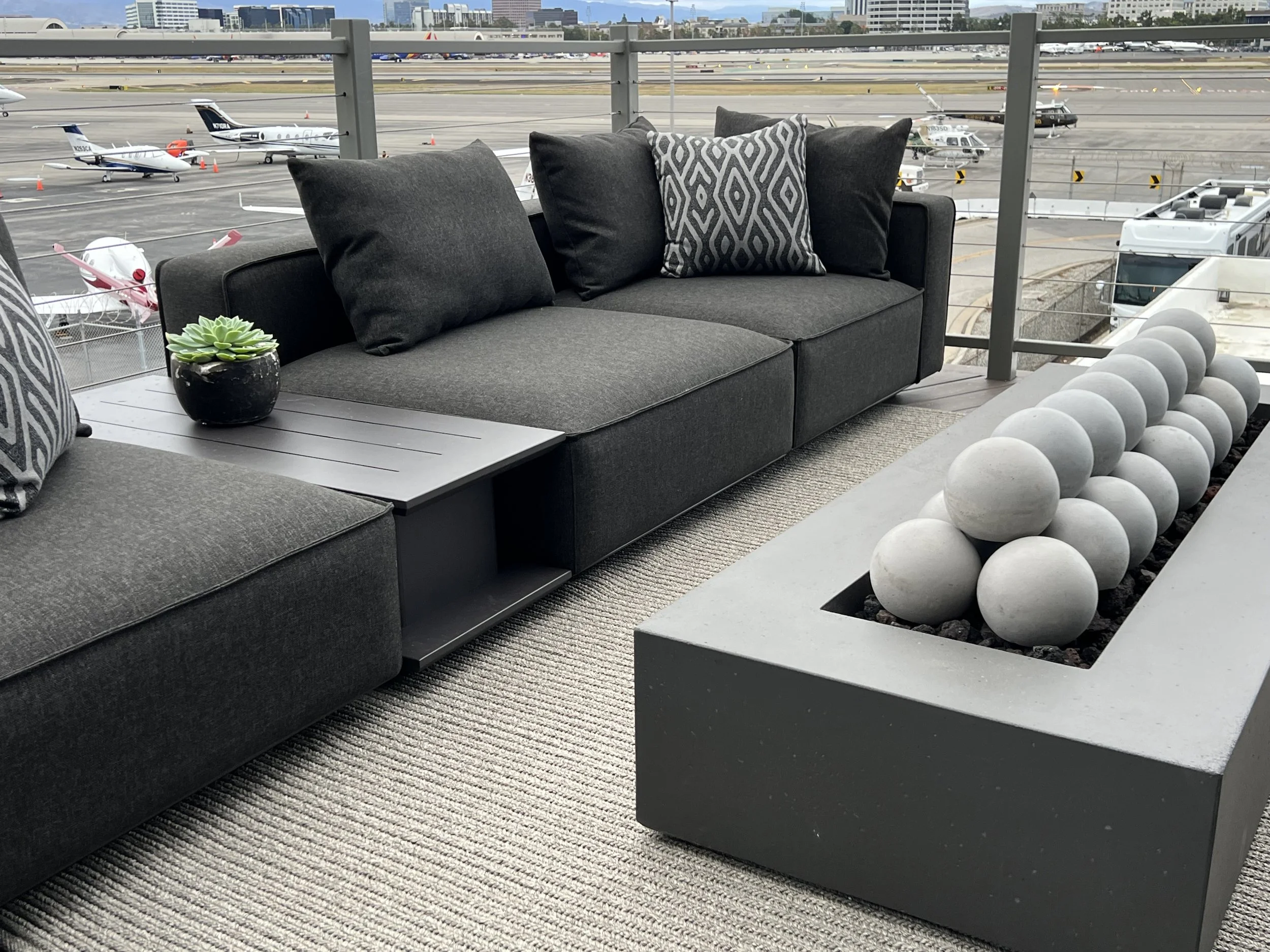 Luxury outdoor sectional with geometric firepit and succulent planter overlooking private runway