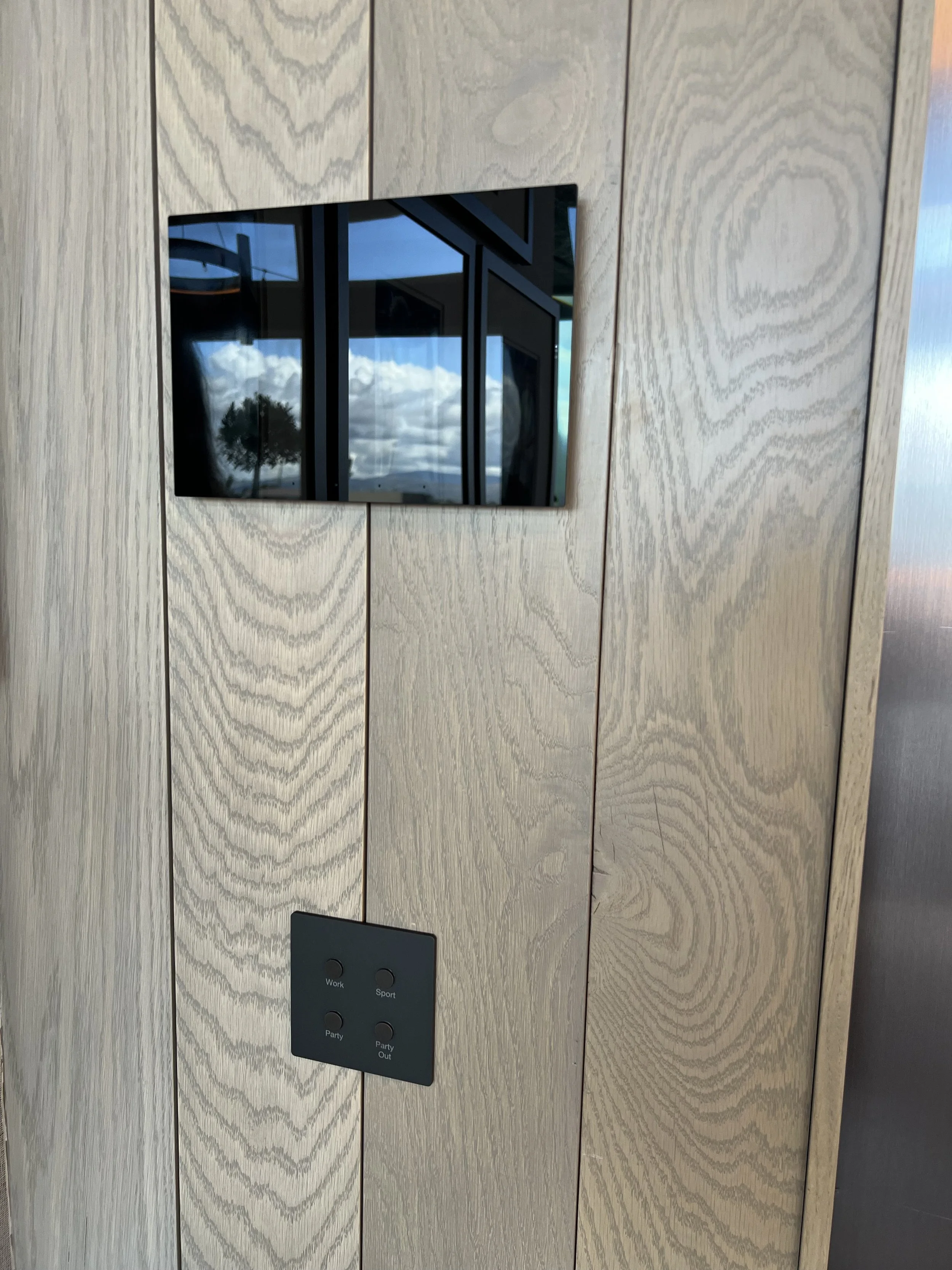 Modern smart wall control panel with lighting and scene buttons on wood-paneled wall in executive office