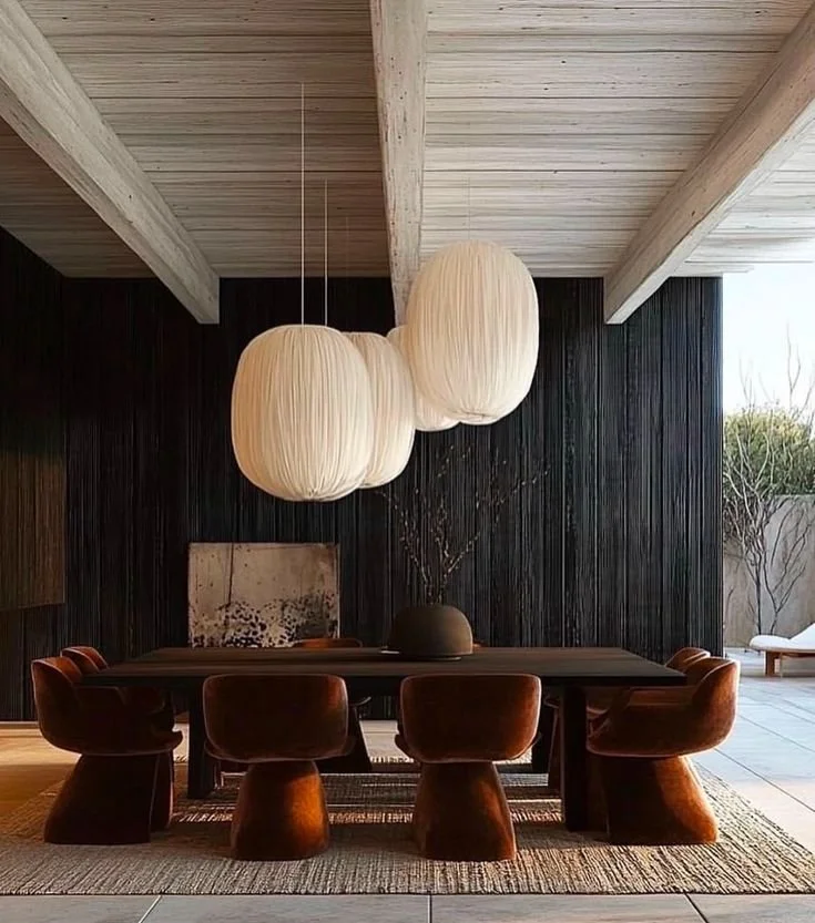 Modern dining room with velvet chairs, oversized fabric pendant lights, and black wood paneling