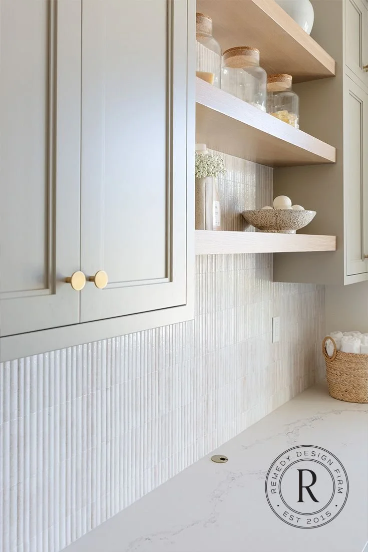 %22Elegant laundry room with vertical white tile backsplash, open wood shelving, minimalist cabinetry, and neutral-toned decor by Remedy Design Firm%22.jpg