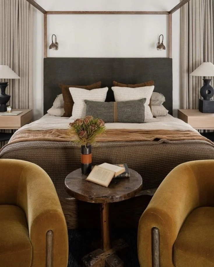 Modern rustic bedroom with canopy bed, mustard velvet chairs, layered neutral bedding, and earthy textures in a cozy, curated layout..jpg
