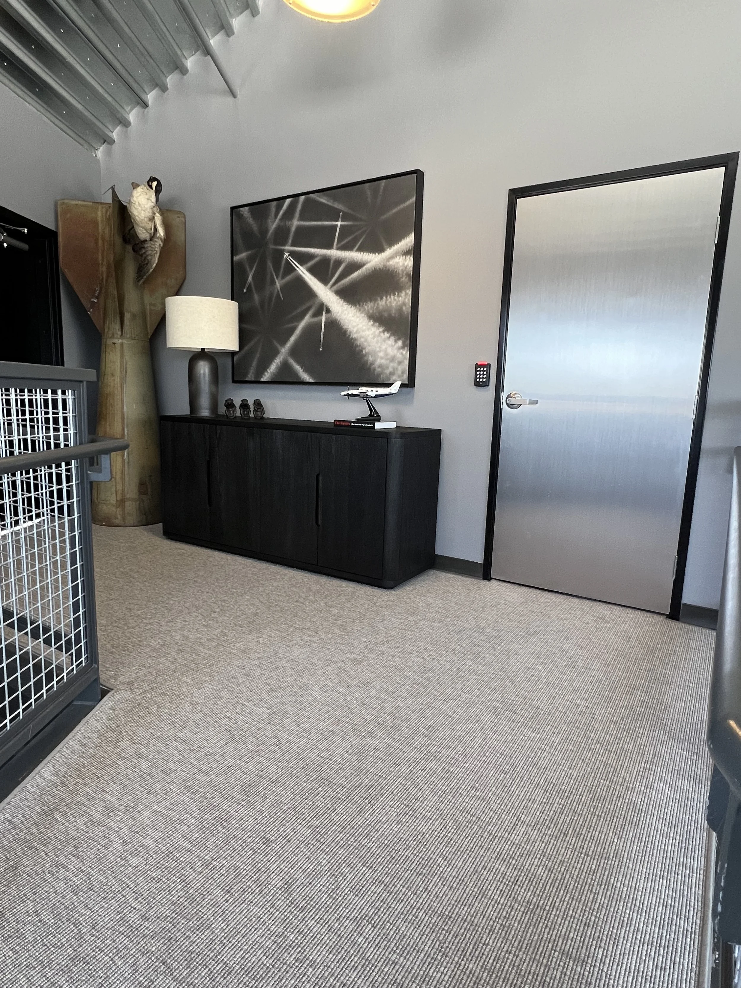 Industrial-modern upstairs landing with aircraft artwork, aviation decor, and custom black console furniture.jpeg