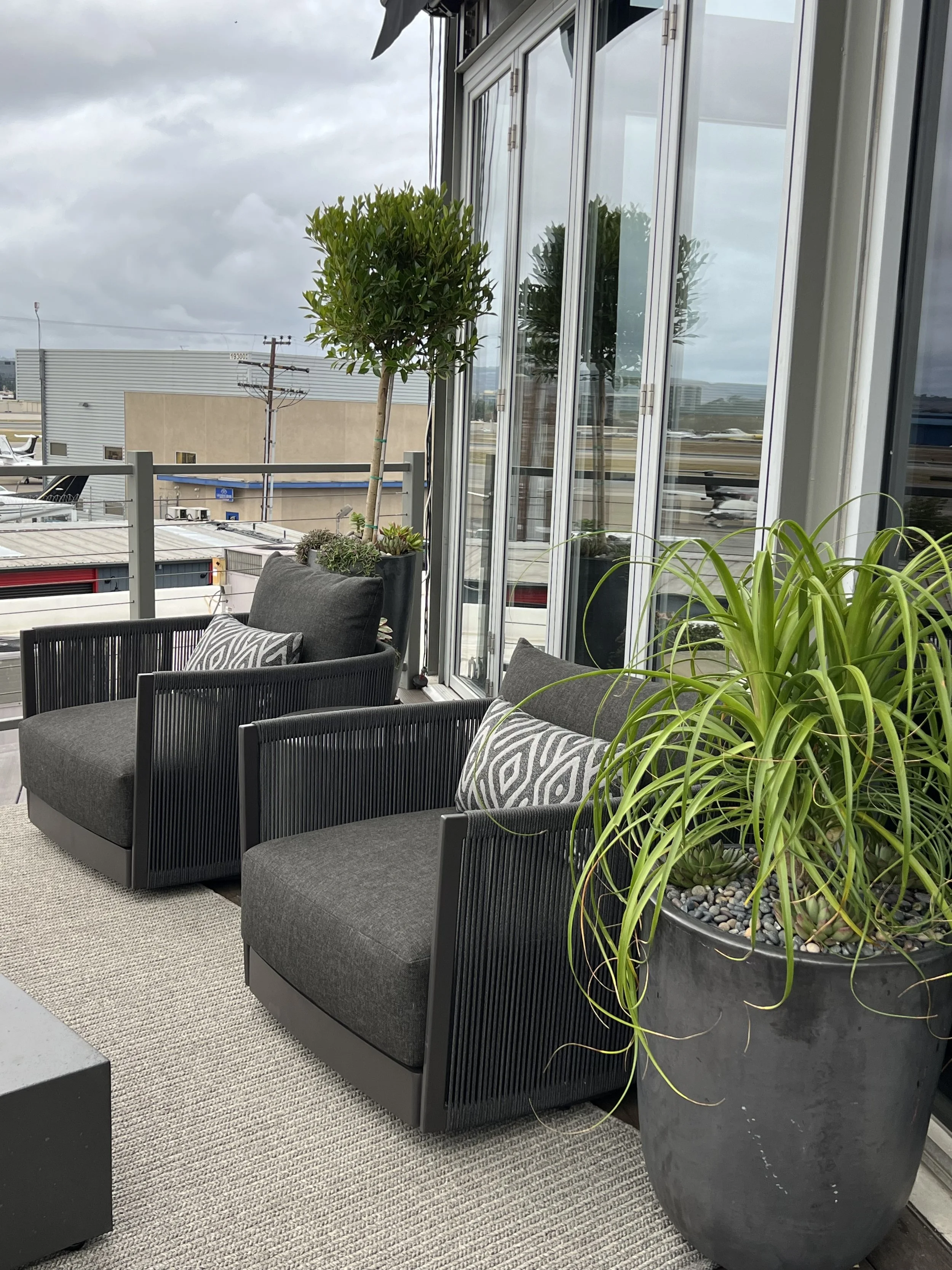 Outdoor airport lounge seating with modern patio chairs, potted greenery, and glass wall exterior at private terminal.jpeg