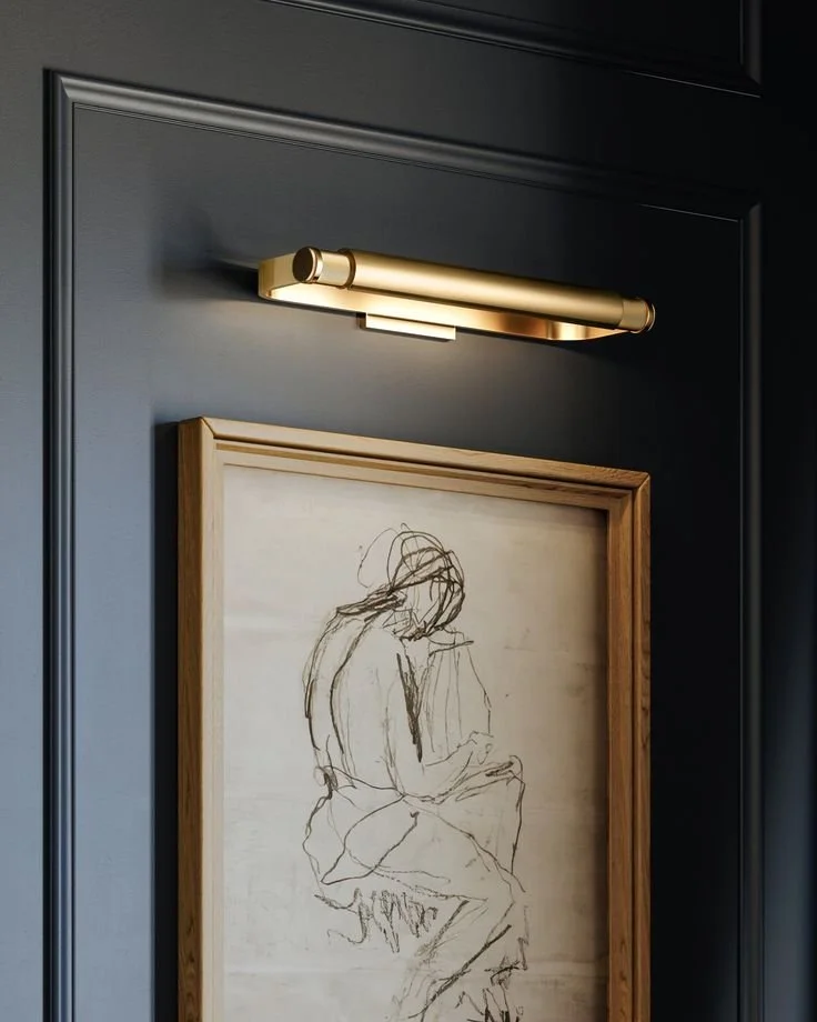Contemporary sketch artwork with sleek gold picture light mounted on navy blue paneled wall"