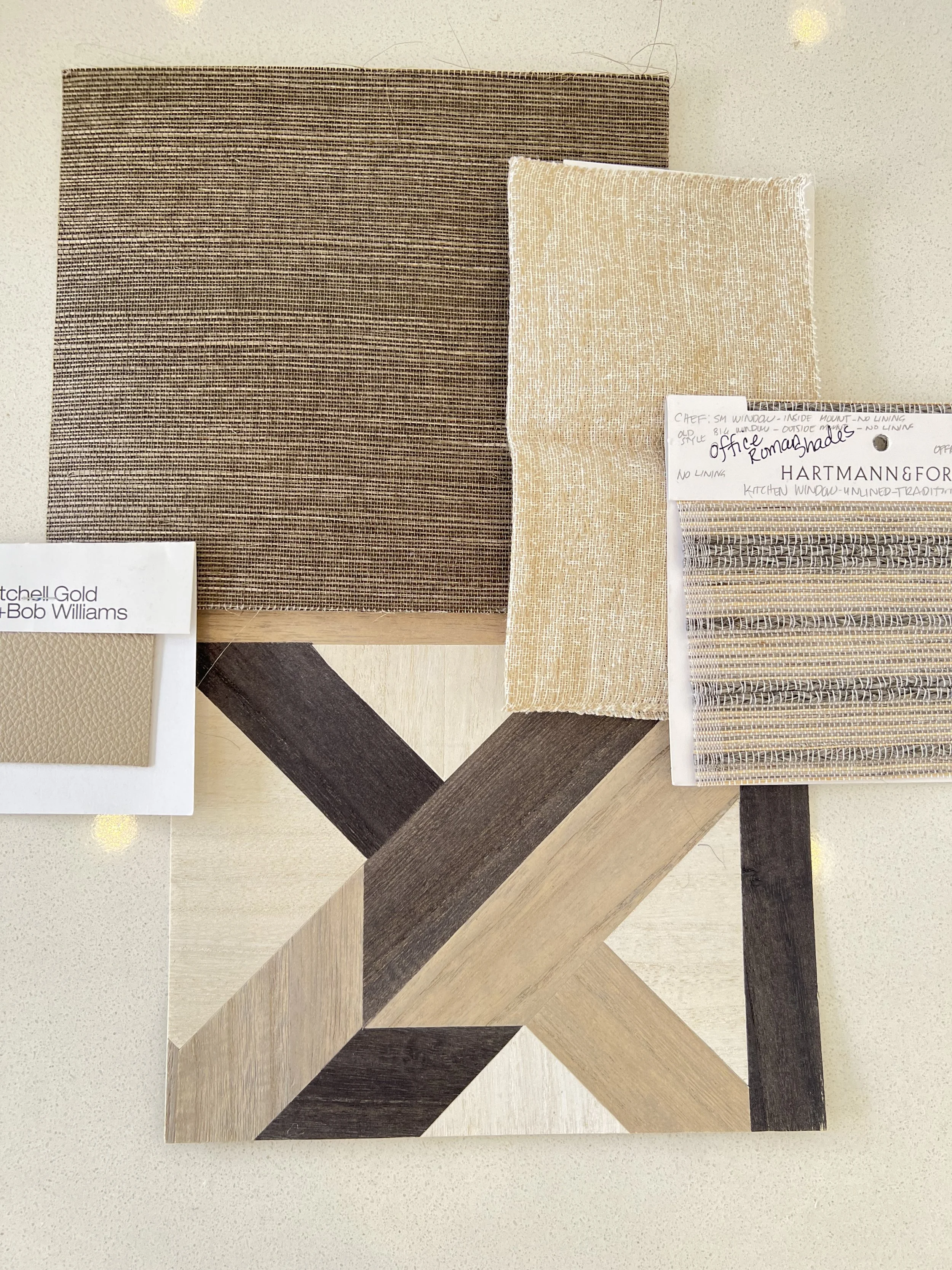Earth-toned interior design mood board with grasscloth wallpaper, wood flooring sample, golden upholstery fabric, and woven shade textile"