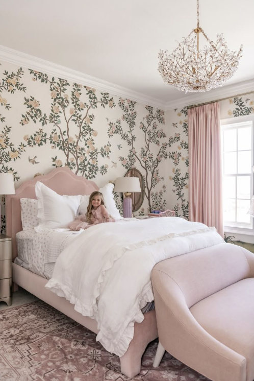 harming girls bedroom with pink upholstered bed, white ruffled bedding, floral wallpaper mural, and crystal branch chandelier"