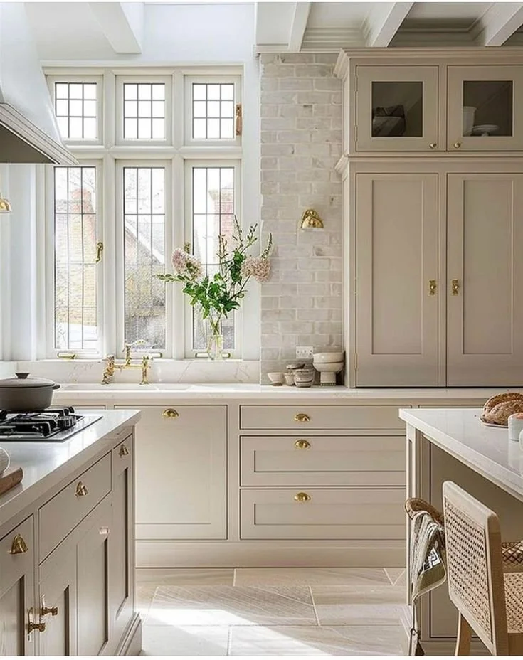 Elegant English-style kitchen with soft taupe cabinets, white brick backsplash, and brass hardware