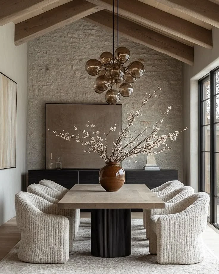 Elegant dining room with vaulted ceiling, stone wall, boucle chairs, and sculptural pendant lighting