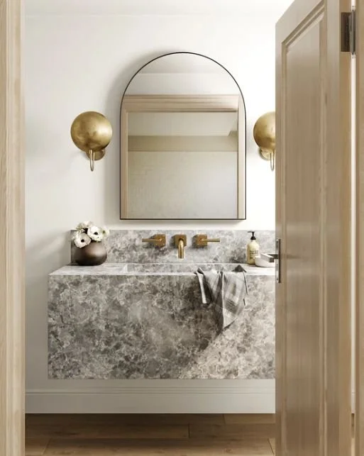 Modern minimalist bathroom with gray marble vanity, gold fixtures, and arched mirror