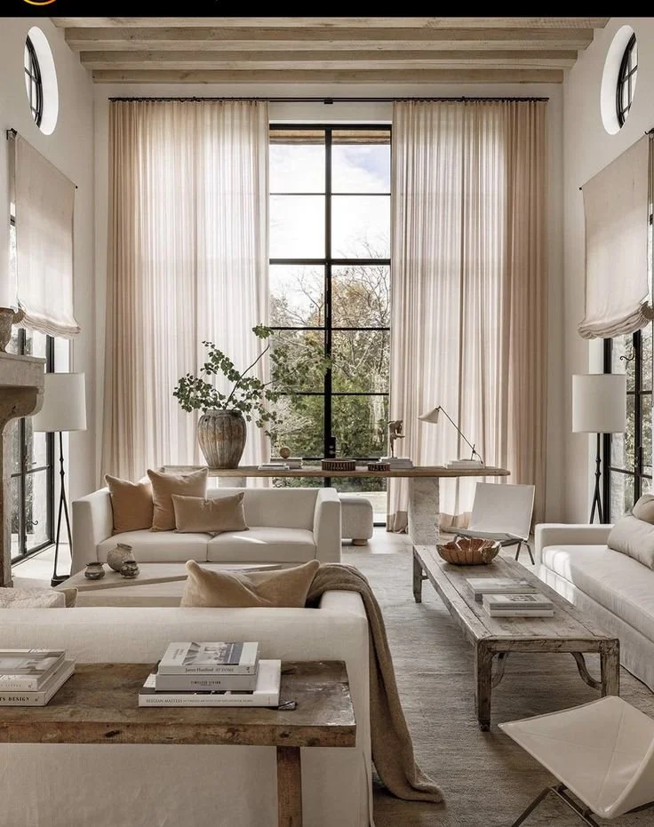 Elegant neutral-toned living room with tall windows, sheer curtains, and rustic wood accents