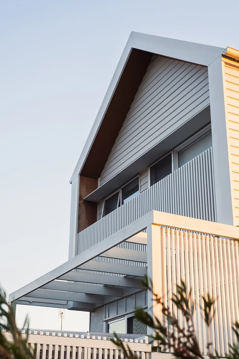 Modern residential building with metal siding, large windows, and a balcony, under a clear sky.