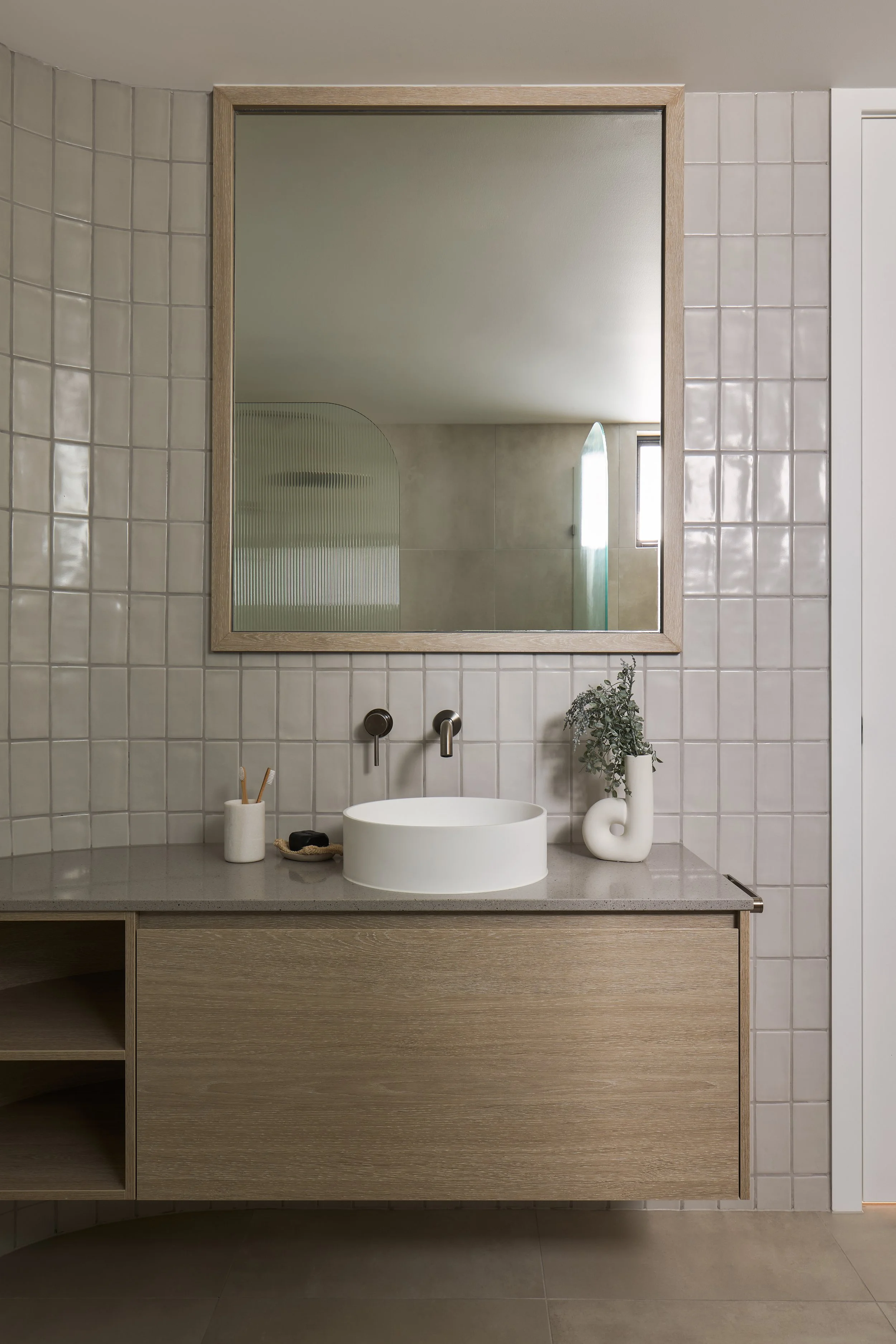 Modern bathroom vanity with a vase and plant, large rectangular mirror, and a round white sink, neutral tones.