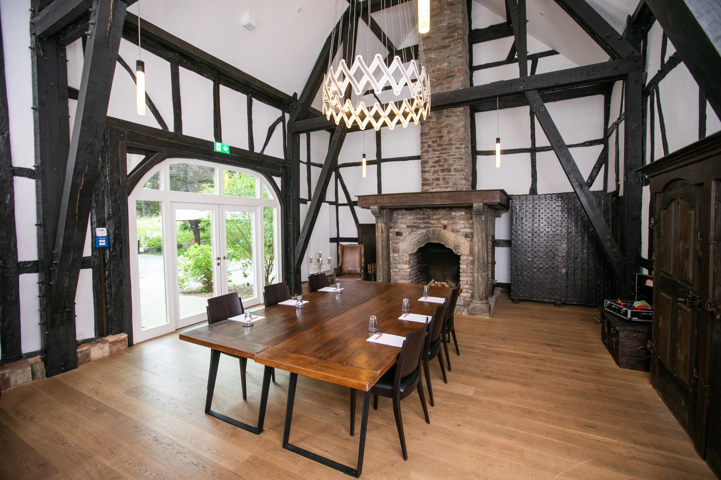 Ein rustikaler Tagungsraum mit einem großen Holztisch, schwarzen Stühlen, einem Kamin, sichtbare Holzbalken und großen Fenstern