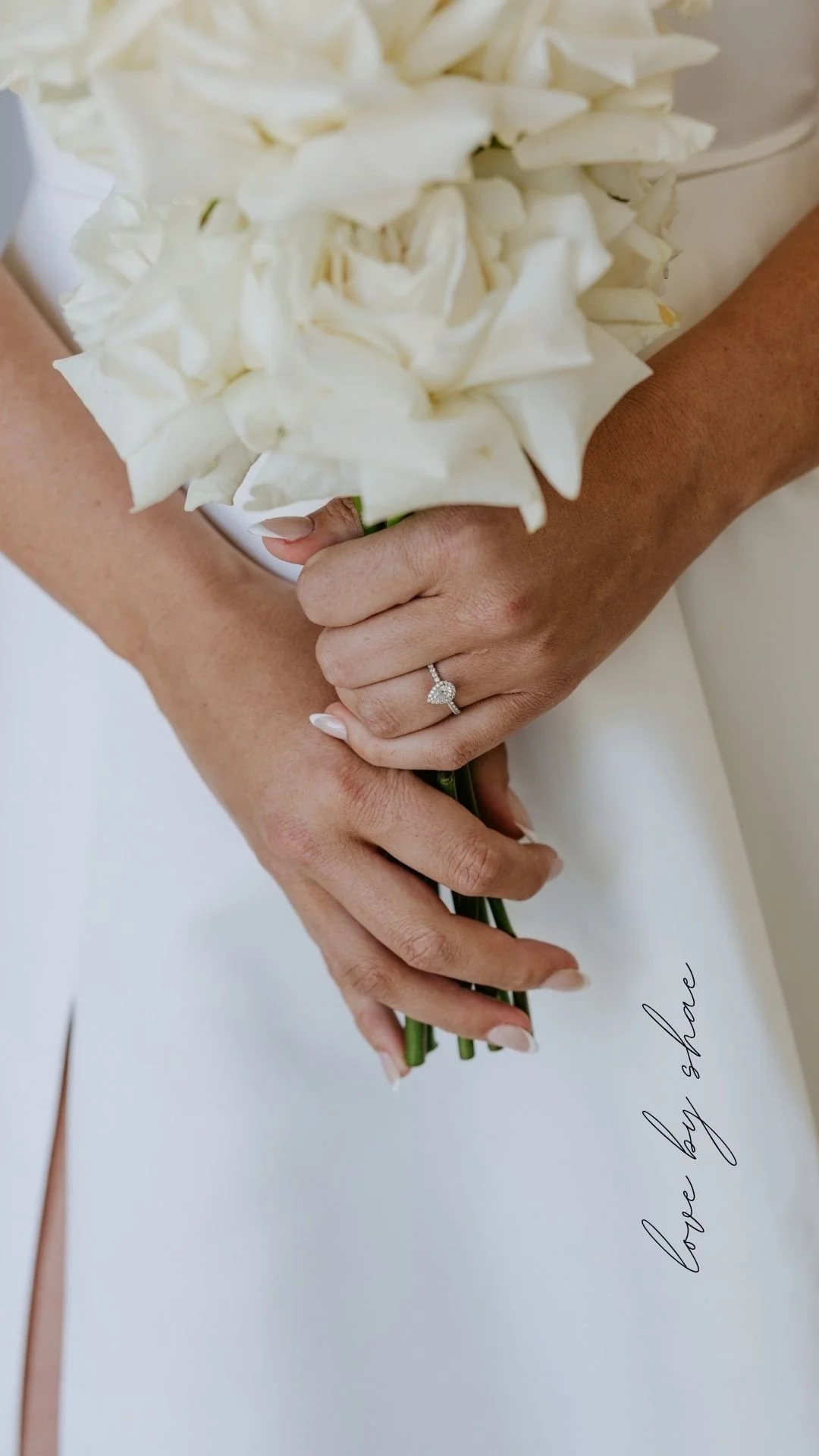 Close-up of a woman holding a bouquet of white flowers, showing her left hand with a diamond engagement ring. There is a handwritten message in the lower right corner of the image.