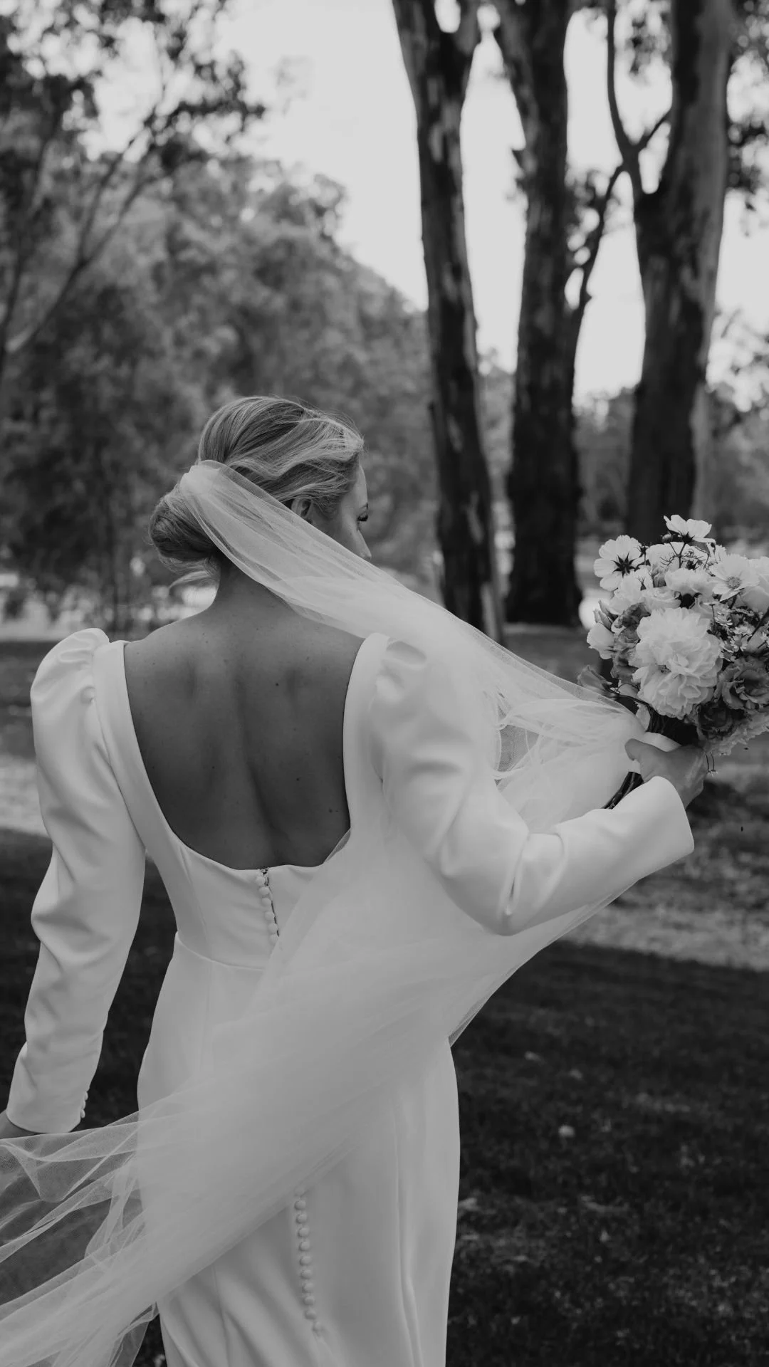 A bride in a wedding gown holding a bouquet of flowers outdoors, with trees in the background.