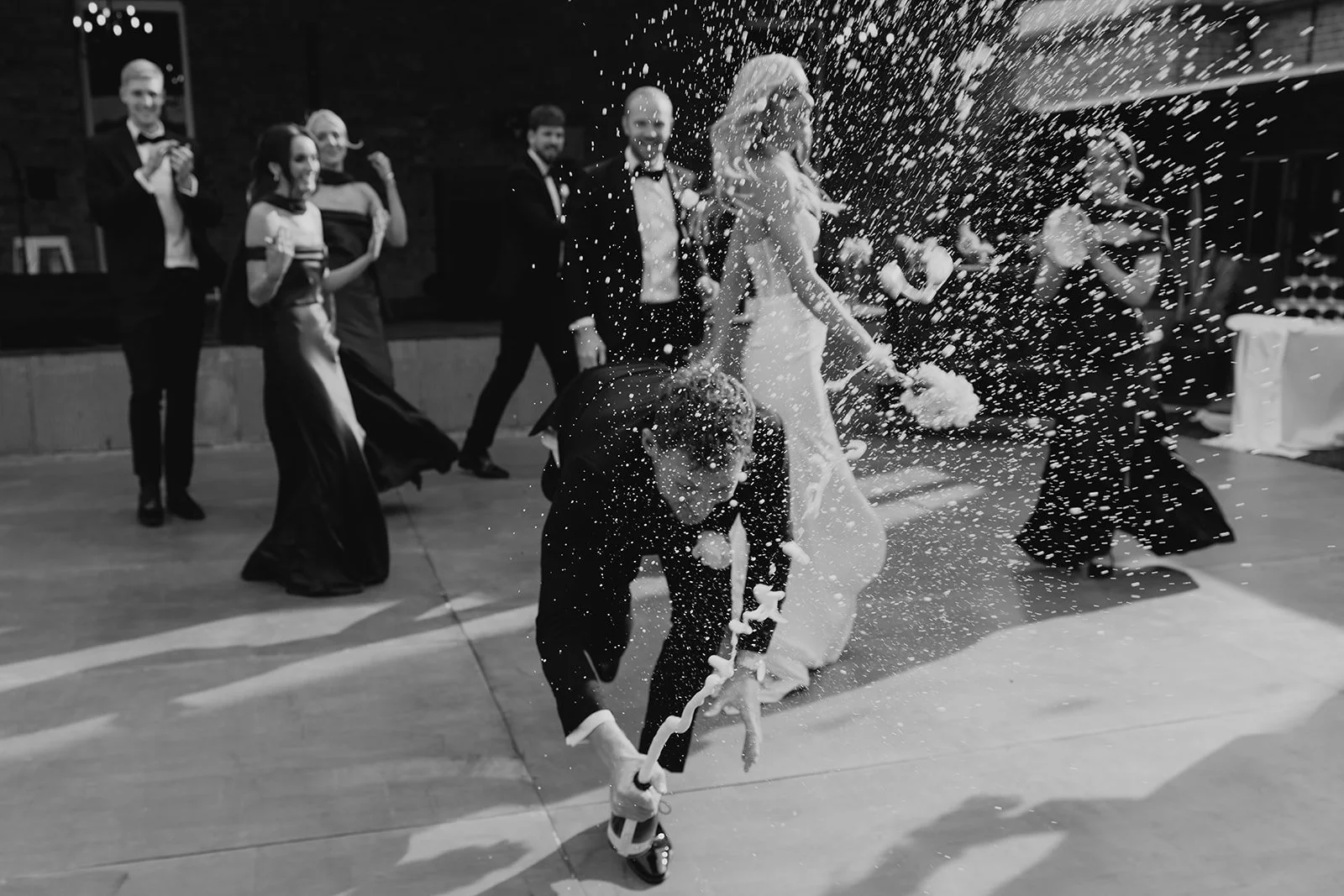 A wedding reception with guests celebrating around the bride and groom. One guest is breaking a piñata, causing candy and treats to fall, while others watch and smile.