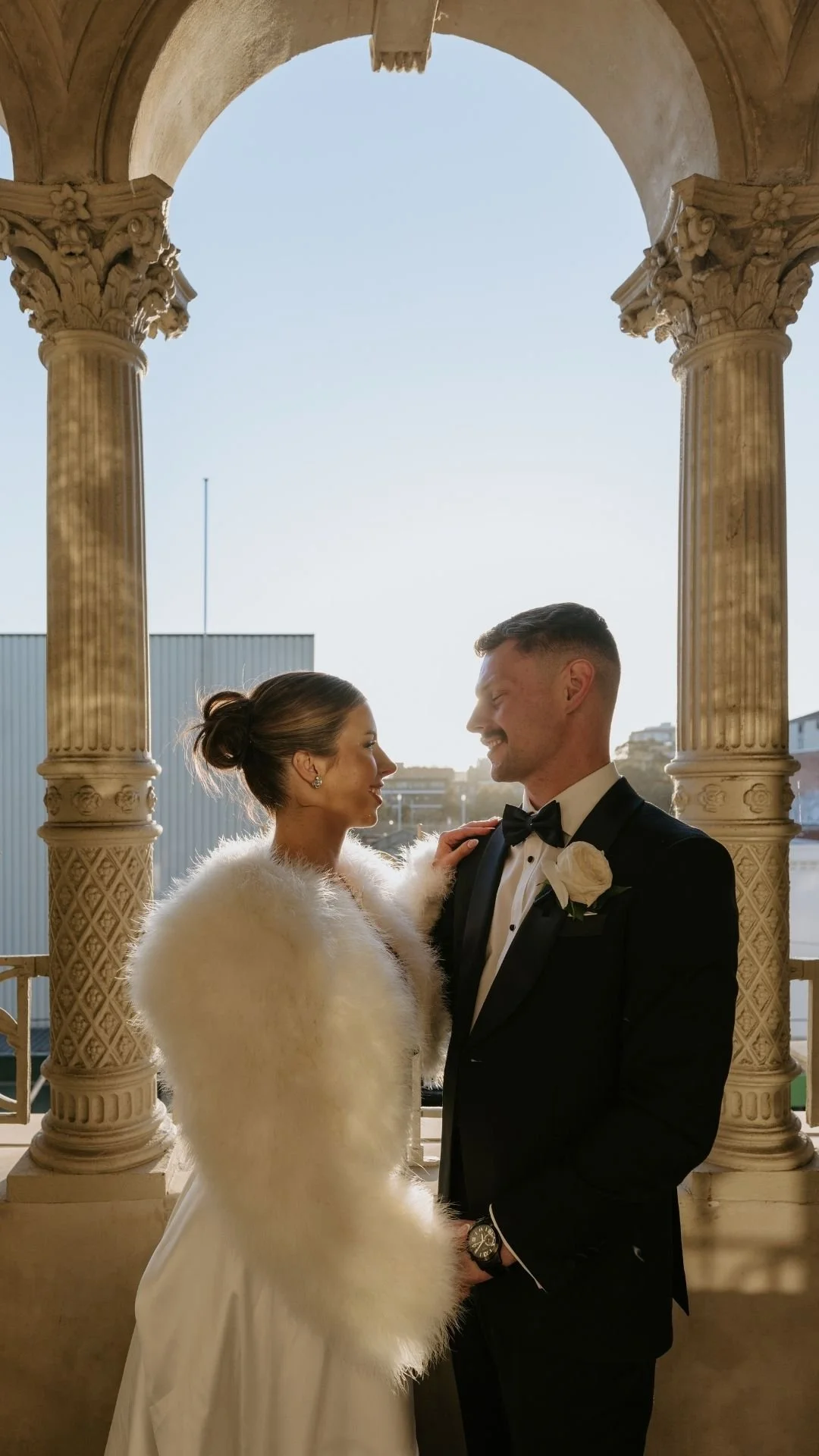 A bride and groom standing together under an ornate archway, smiling at each other during their wedding celebration.