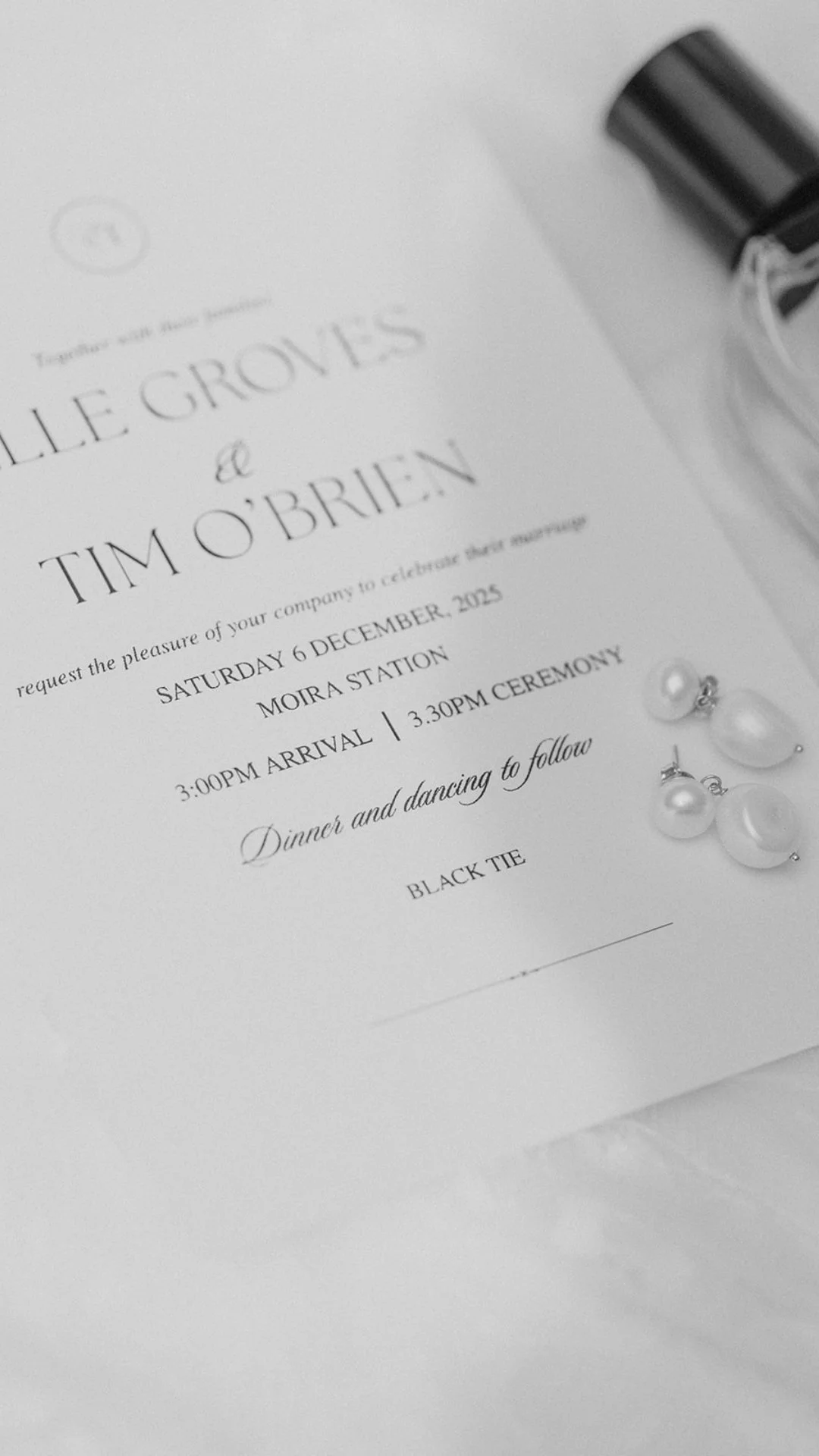 A wedding invitation for Elle Groves and Tim O'Brien, featuring elegant black and white text, pearl earrings, and a black tie on a white surface.