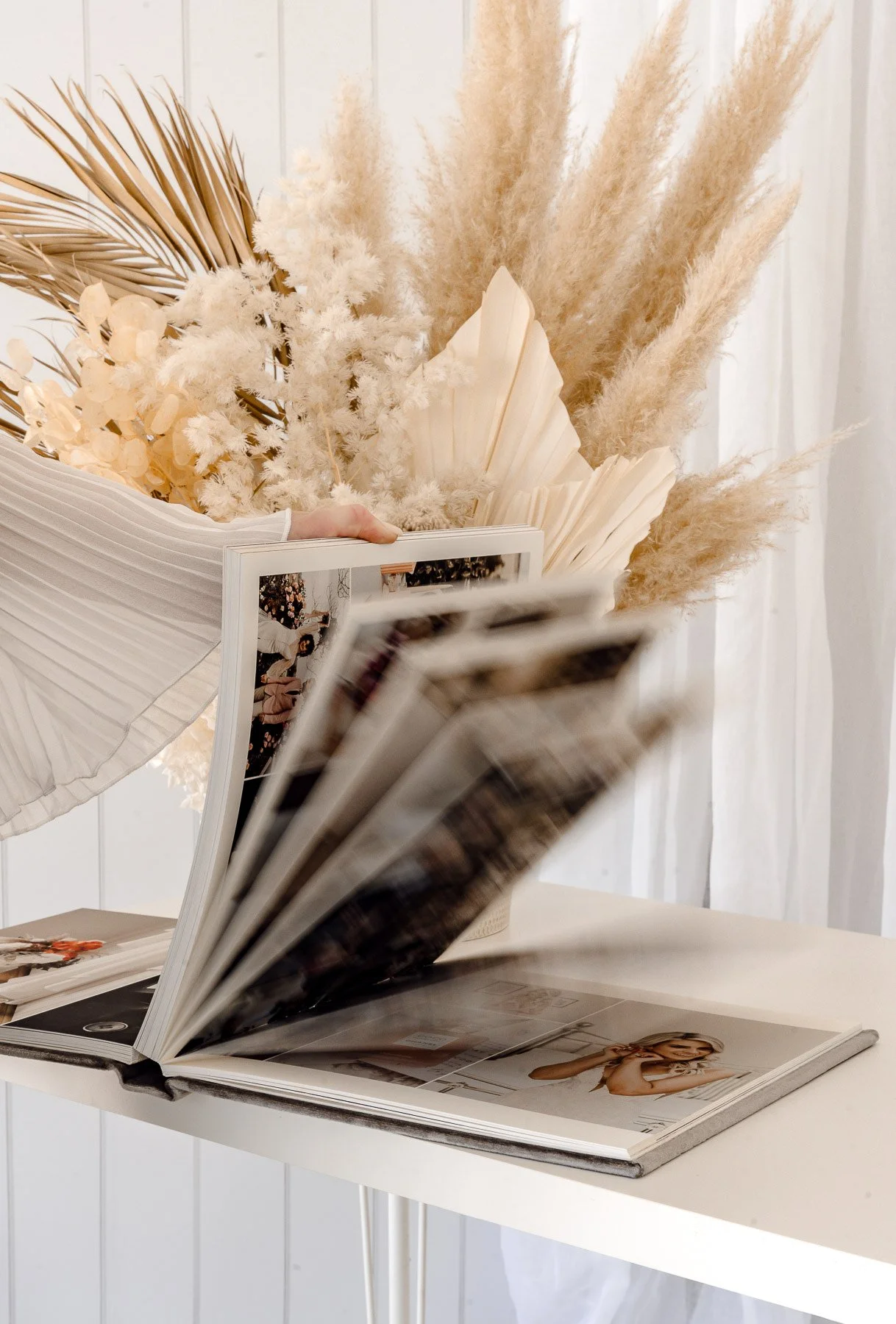 Open magazine on a white table with black and white photos, a bouquet of dried beige and white flowers and pampas grass in the background.