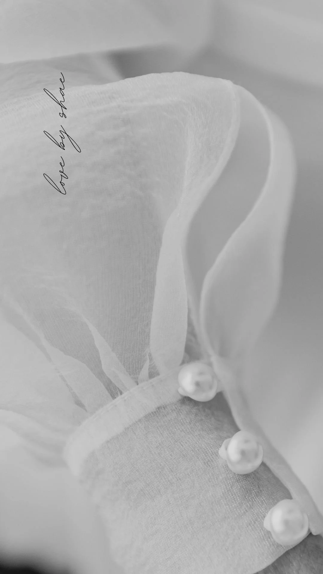 Close-up of a white flower, possibly a rose, wrapped in fine transparent fabric with small beads along the edge. The words "love by share" are written in cursive on the fabric.