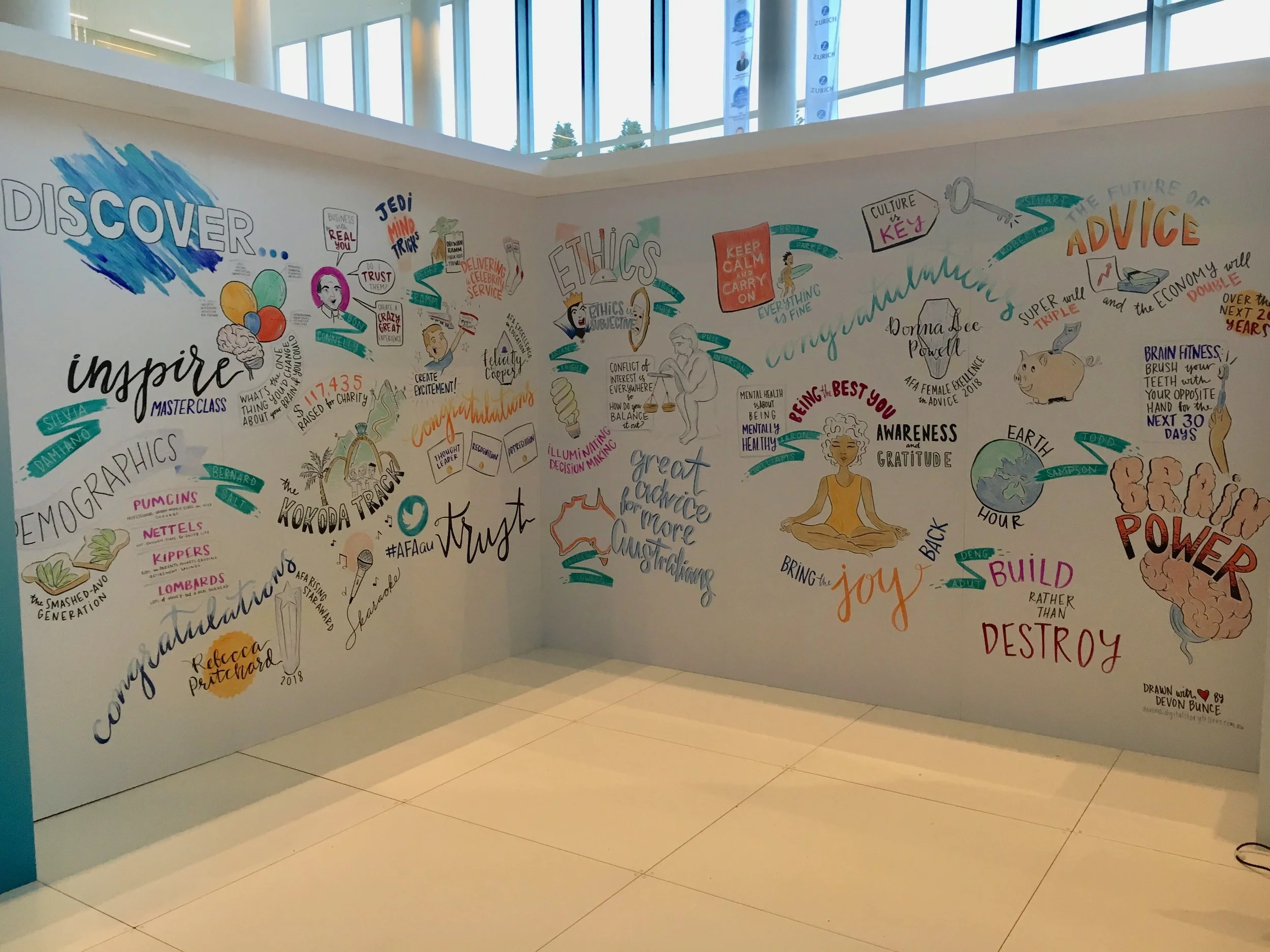 Colorful mural with words and illustrations promoting inspiration, ethics, empowerment, and mindfulness, including phrases like 'Discover,' 'Inspire,' 'Power,' and 'Trust,' along with images of a brain, Earth, a brain with clouds, a person meditating