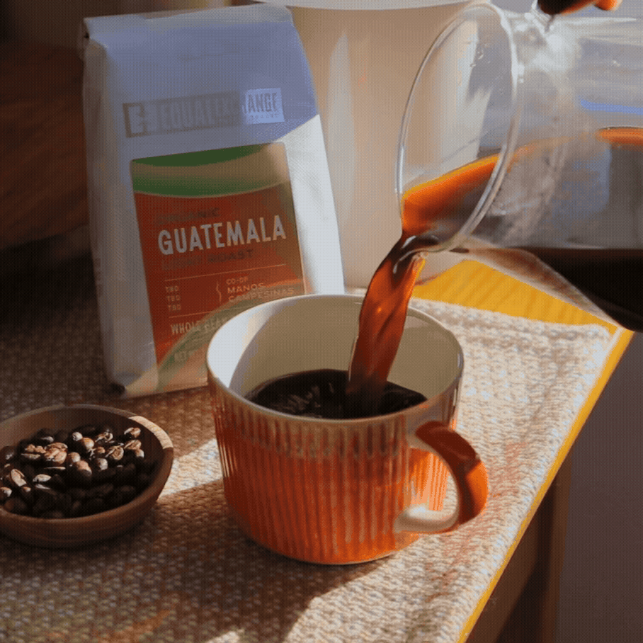 pouring coffee into an orange mug with bag of Guatemala in background