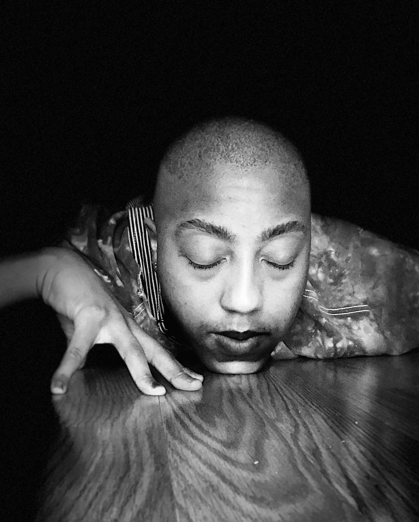 A person with short hair resting their head on a wooden surface with their eyes closed.