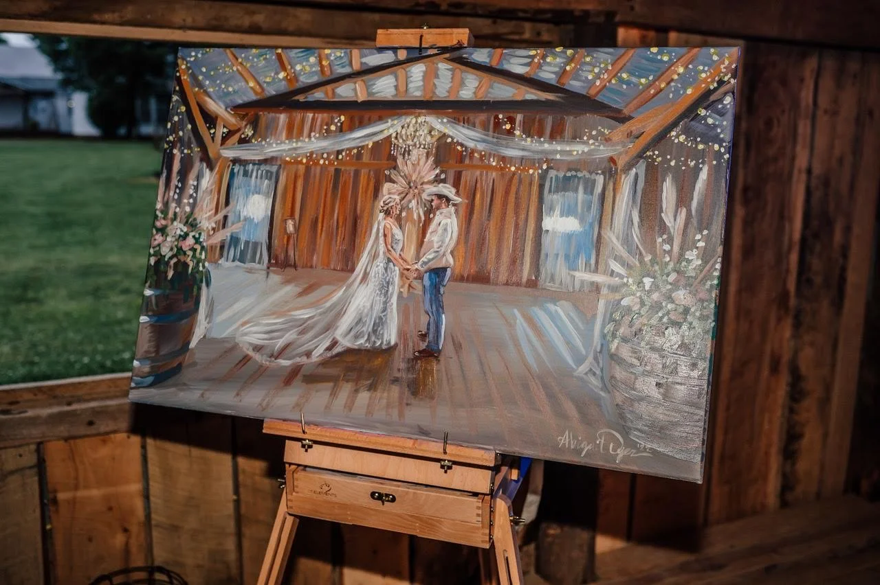Hand-painted wedding scene depicting a couple holding hands inside a rustic barn with string lights, on display on an easel.