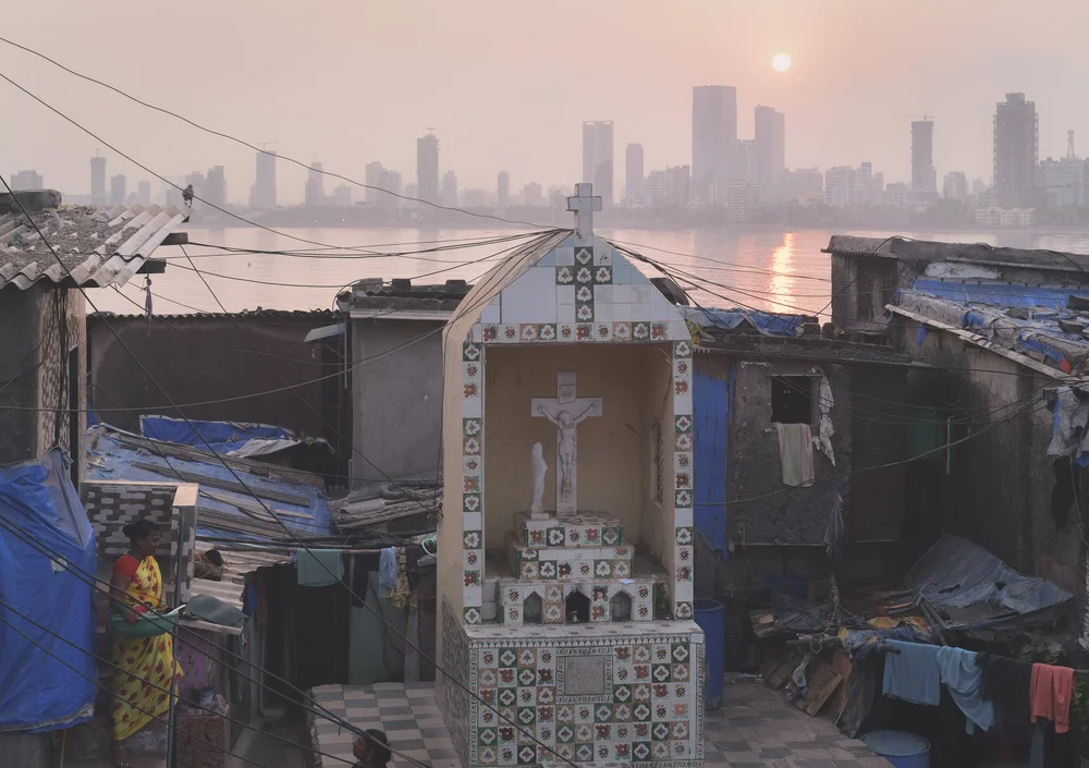 A whitewashed roadside shrine among Mumbai homes, towers in the haze behind